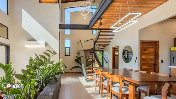 A dining area with a long wooden table sits beneath an open staircase.