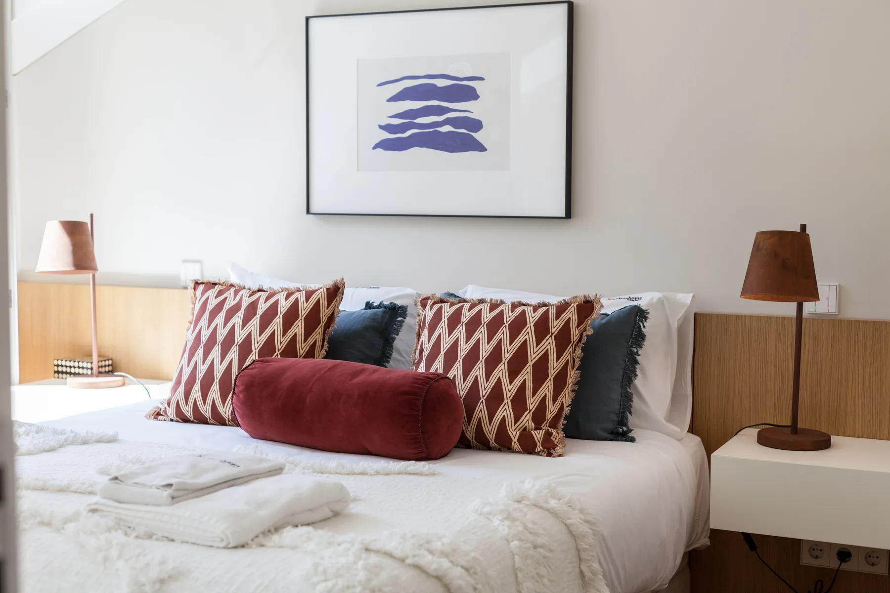 A bedroom with a neatly made bed, patterned cushions, and bedside lamps.