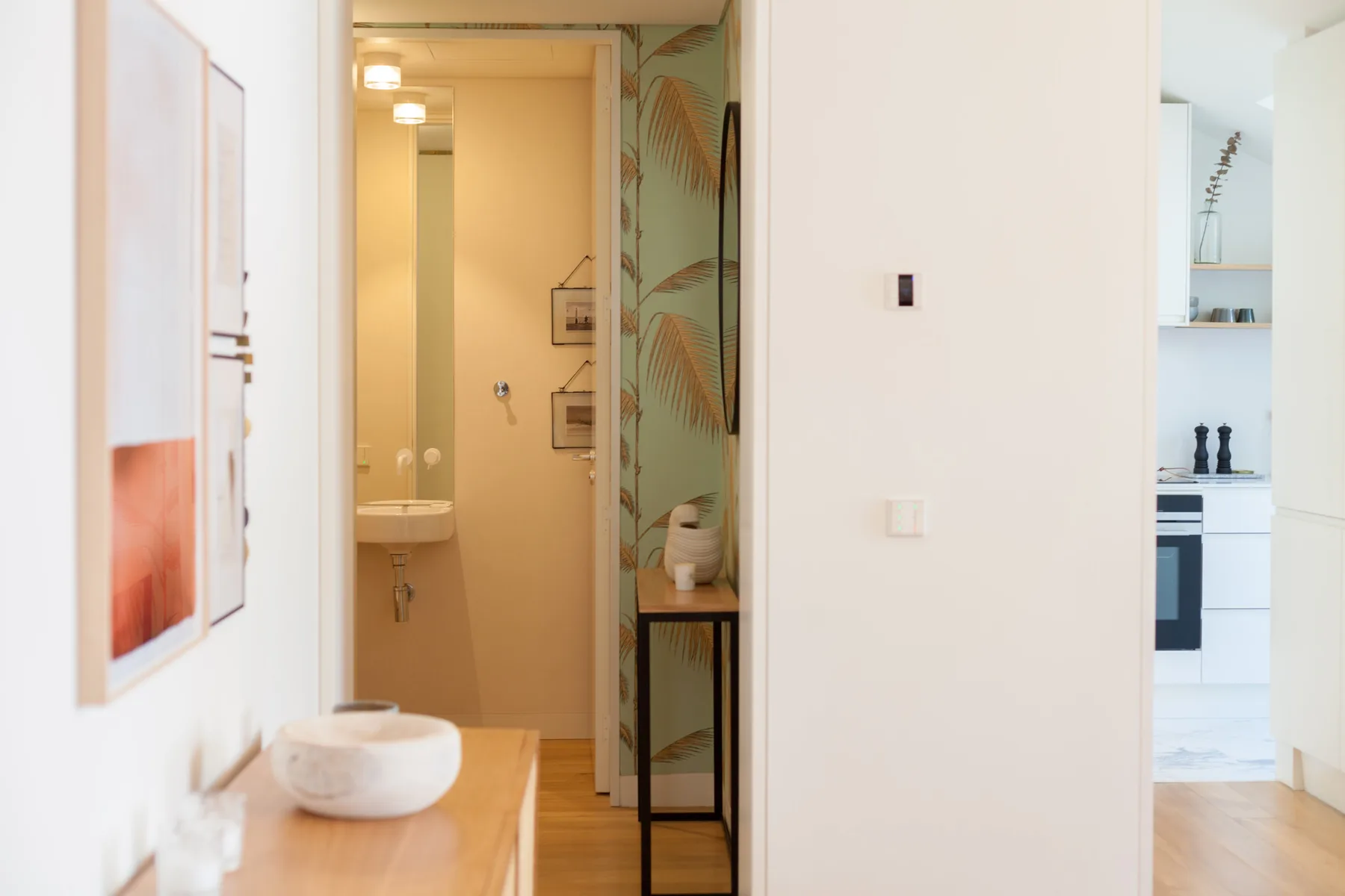 A bright apartment interior shows a hallway leading to a bathroom and kitchen.