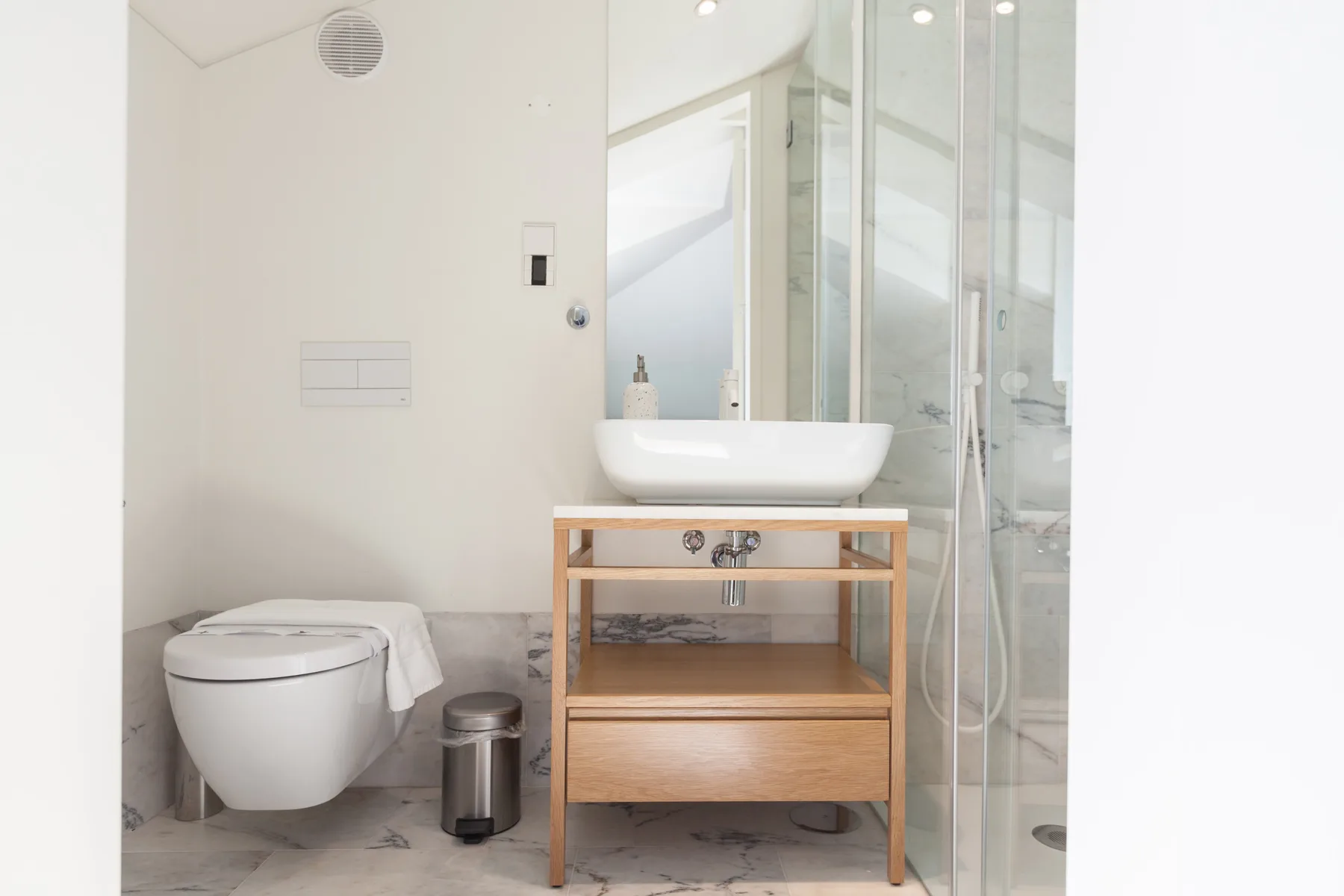 A bathroom with a wall-mounted toilet, vessel sink, and glass shower.