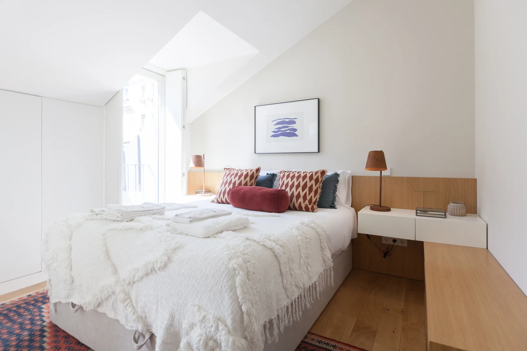 A bright bedroom with a bed, bedside tables, and a framed print.