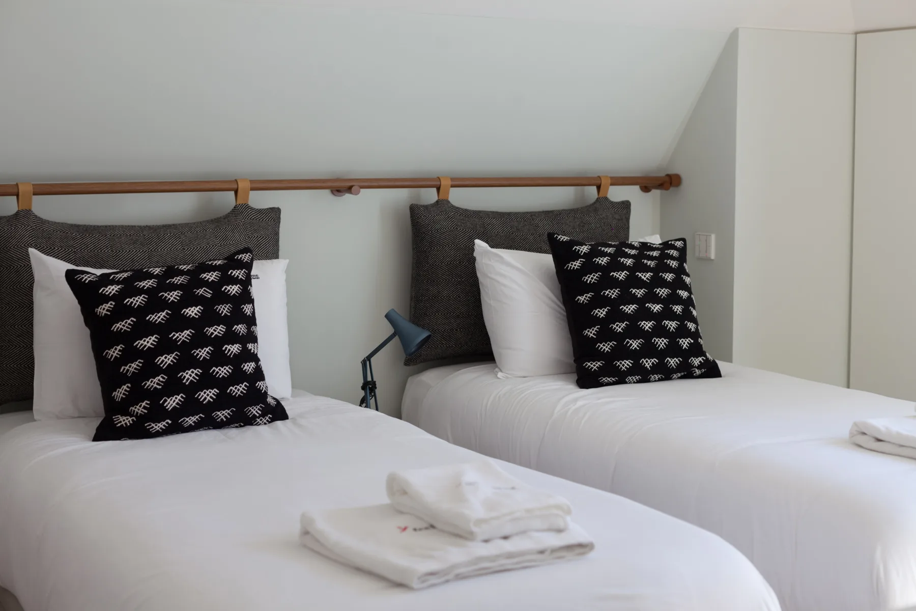 A bedroom with two beds dressed in white linens and dark patterned pillows.