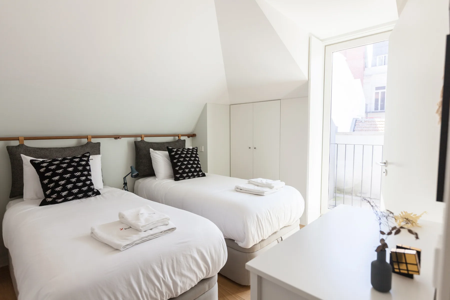A bright bedroom with two beds and an open door to a balcony.