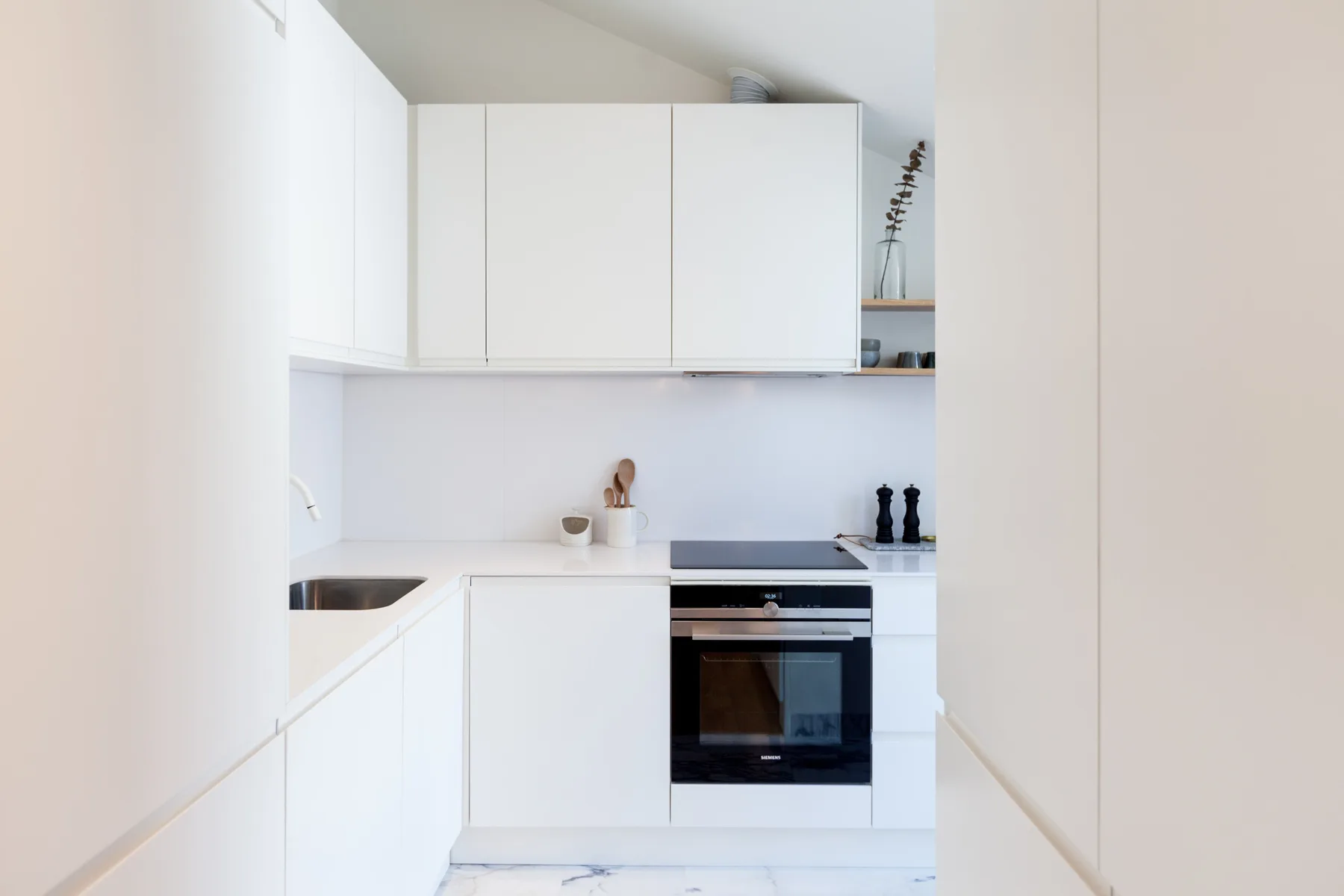 A bright white kitchen with cabinets, a countertop, and a built-in oven.