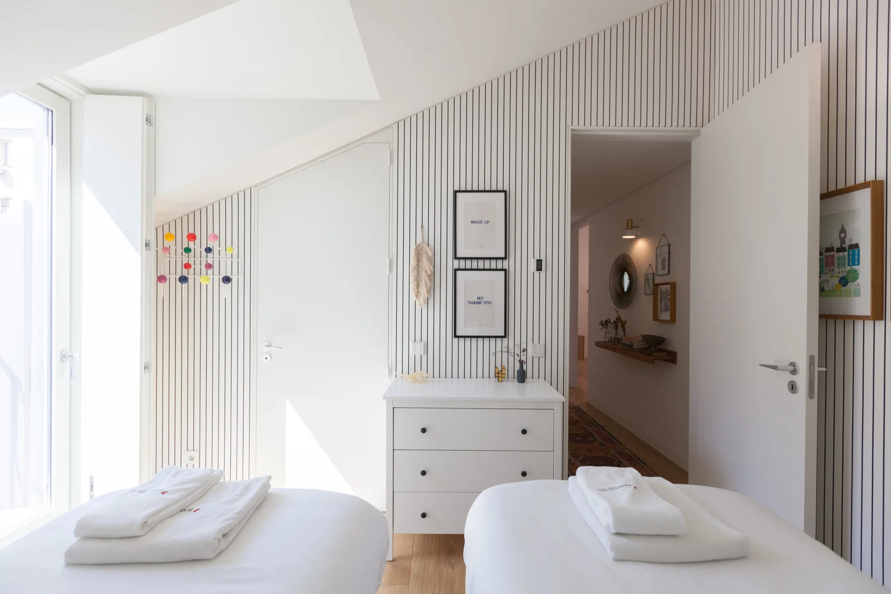A bright bedroom with two beds, a dresser, and an open doorway.