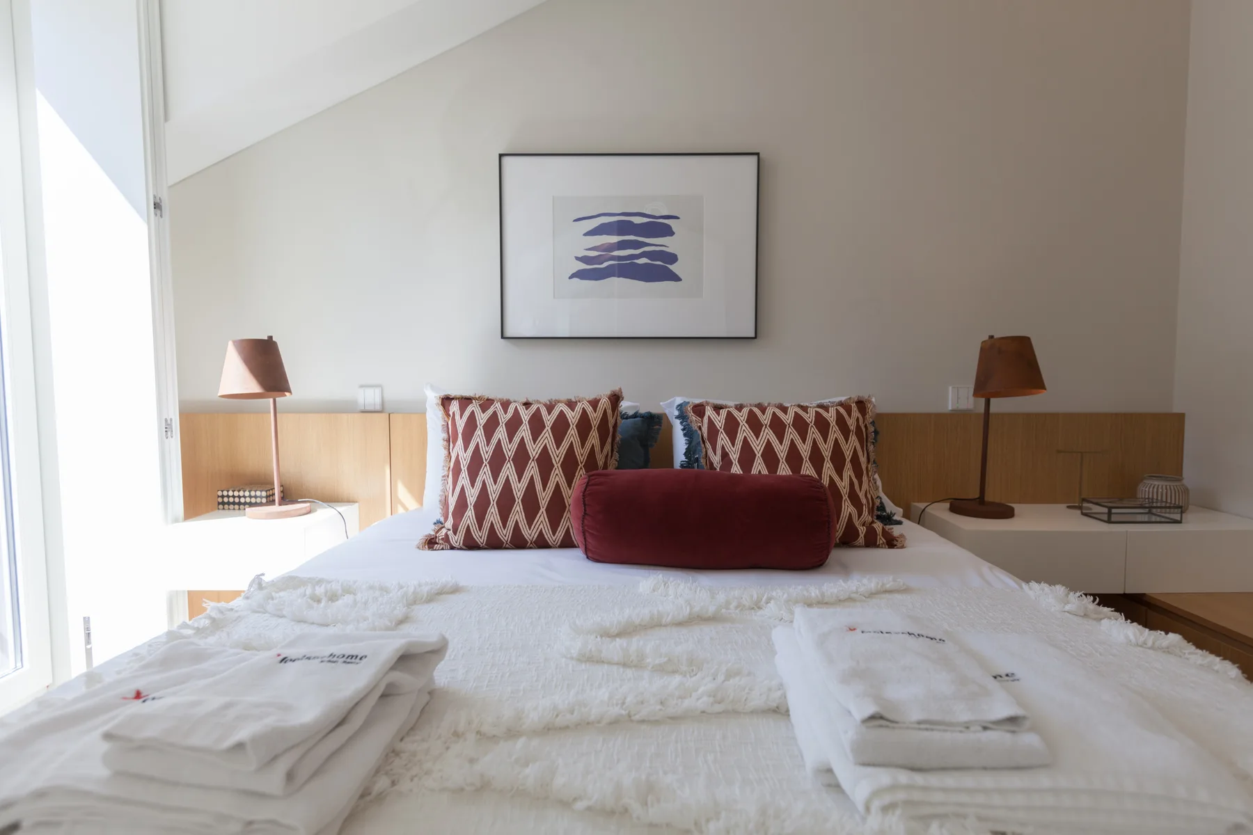 A bedroom with a neatly made bed and framed artwork above it.