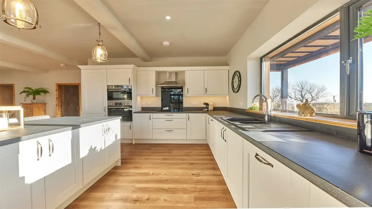 A bright kitchen with white cabinetry, dark counters, and a large window.