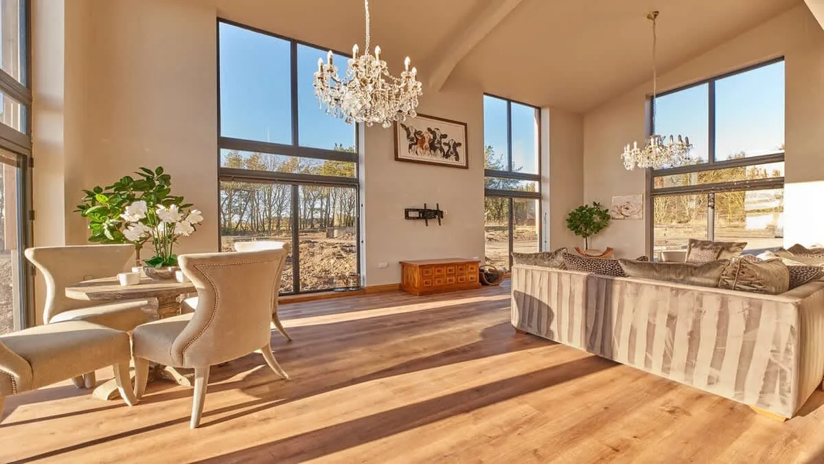 A bright living room with large windows, seating, and chandeliers.