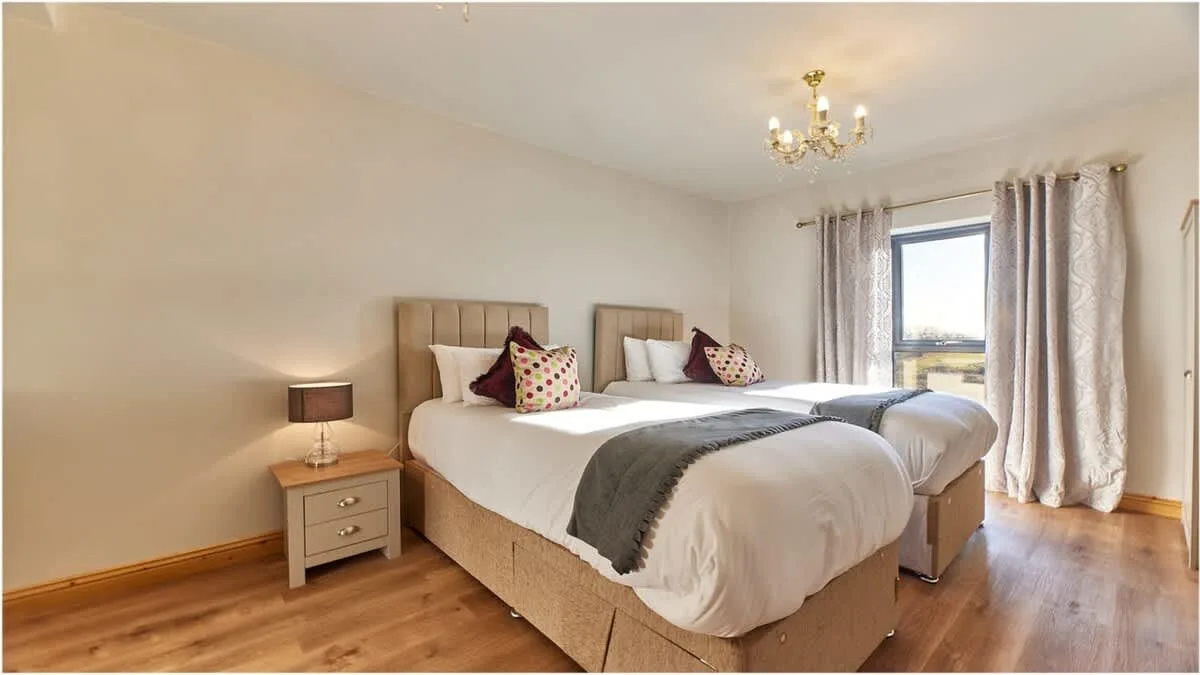 A bedroom with two beds, bedside tables, and a curtained window.