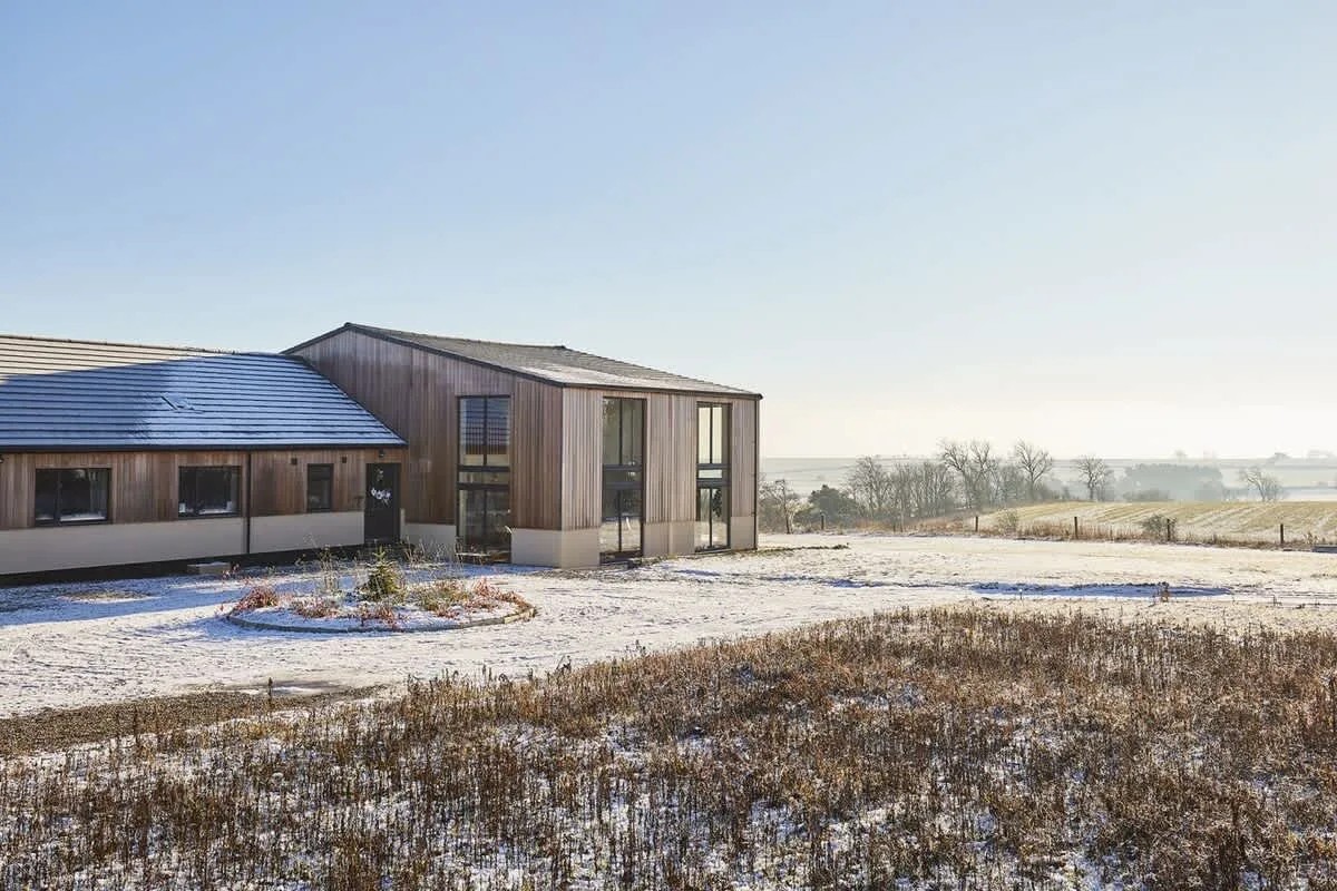 A modern building stands beside a snow-dusted field under a clear sky.