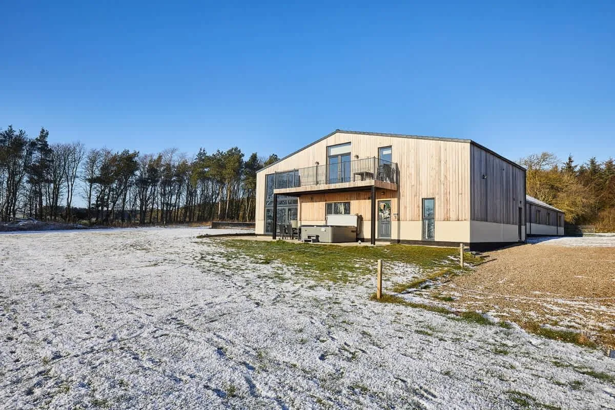 A modern wood-clad building stands beside a broad, lightly snow-covered lawn.