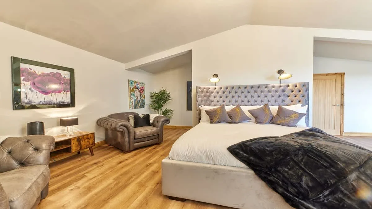 Bedroom with a large bed, upholstered seating, and framed wall art.
