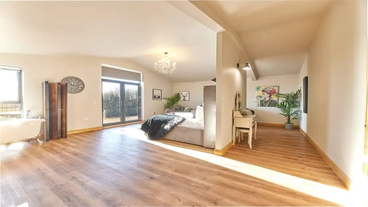 A bedroom with a bed, wooden flooring, and a small desk.