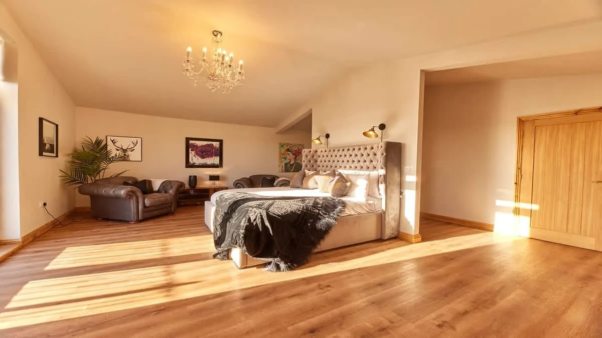A bedroom with a bed, seating area, and wooden flooring.