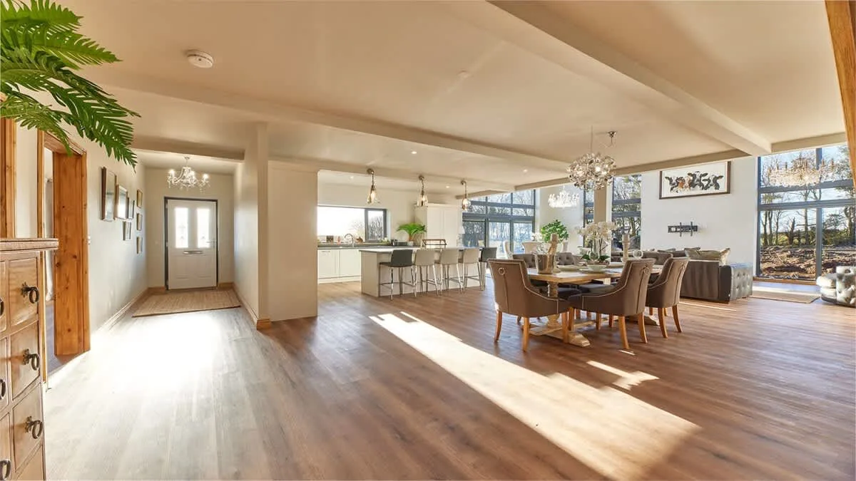 An open-plan dining and kitchen area with a large table and windows.