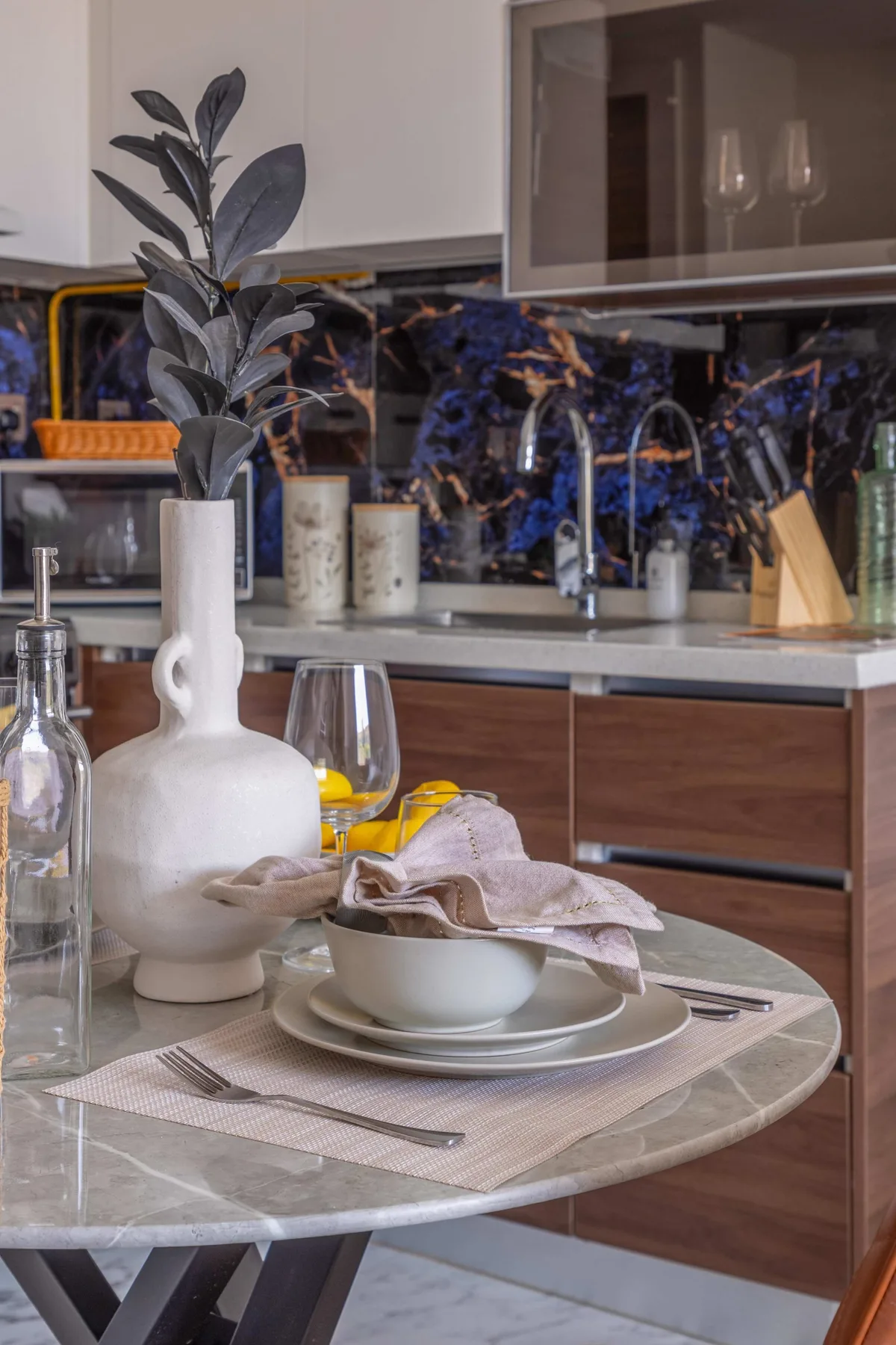 A dining table set with plates and a vase stands in front of a kitchen.