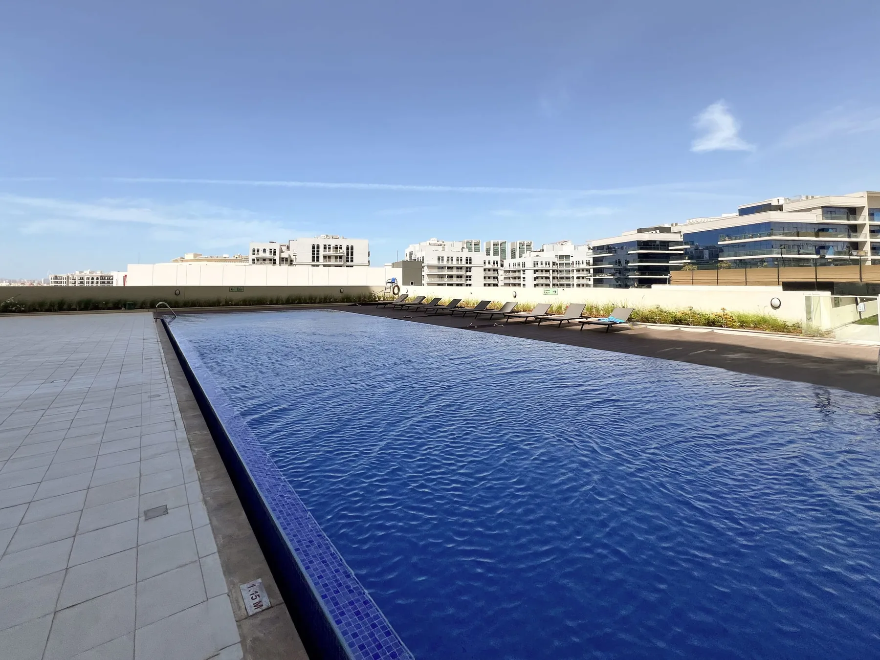 An outdoor swimming pool with a tiled deck and buildings in the background.