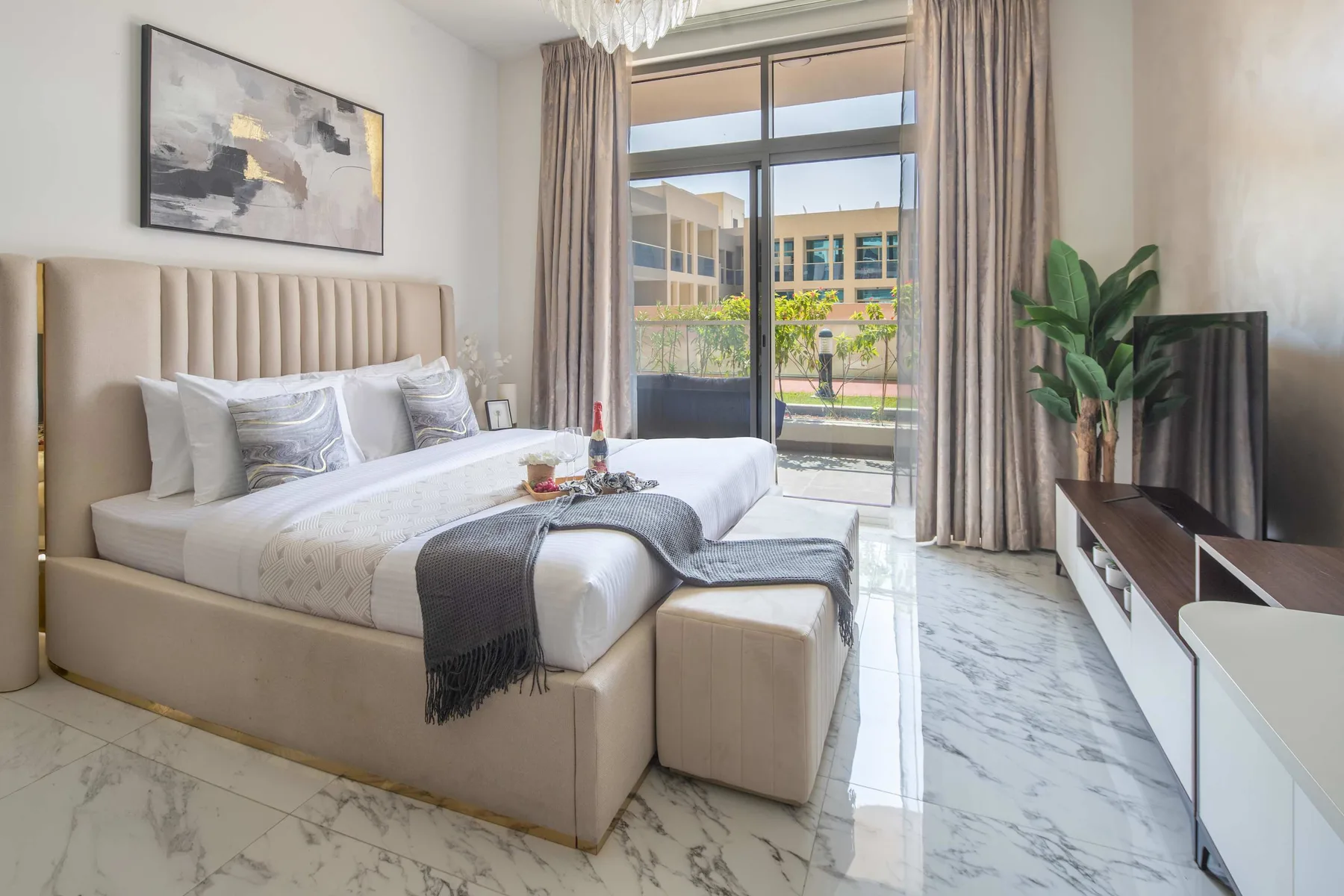 A bright bedroom with a large bed, a television, and a balcony window.