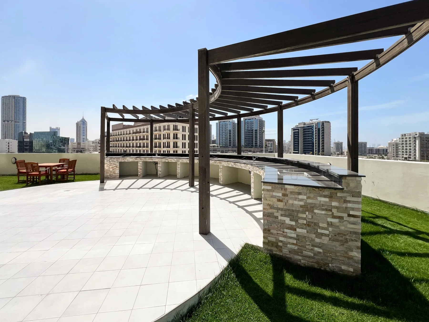 A rooftop terrace with a shaded pergola, paved seating area, and city skyline.