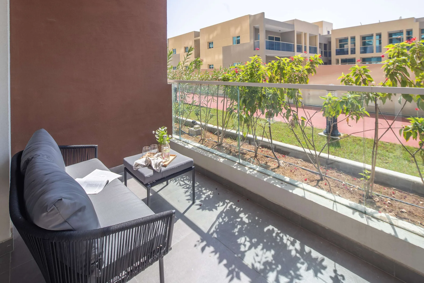 A balcony seating area overlooks a landscaped courtyard and nearby building.