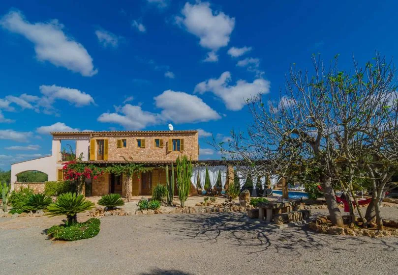 Una casa de piedra se alza junto a un patio ajardinado con árboles y asientos al aire libre.