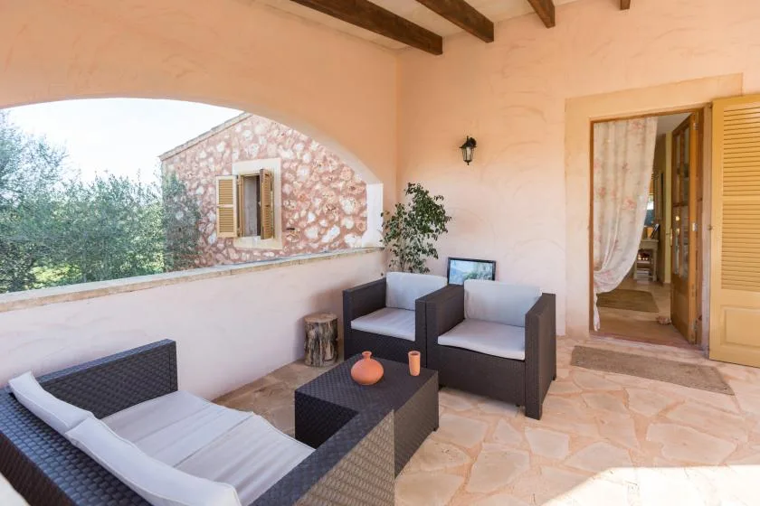 Un patio cubierto con asientos acolchados y una abertura en arco con vistas a la vegetación.