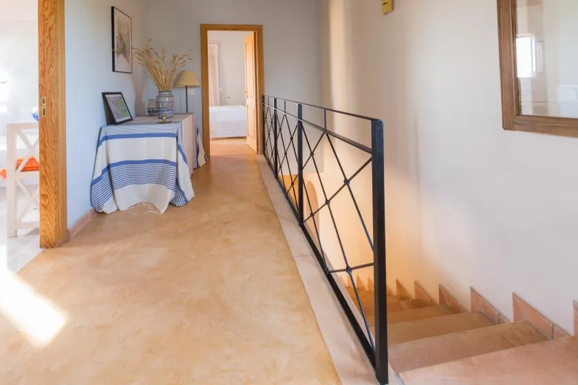 Un pasillo luminoso con una mesa pequeña y una escalera detrás de una barandilla negra.