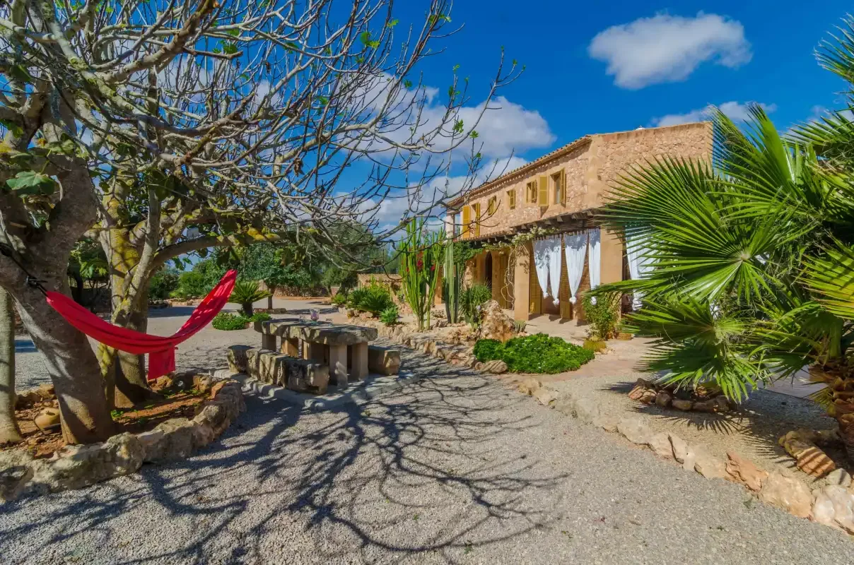 Un patio soleado de piedra con una hamaca roja y árboles frondosos.