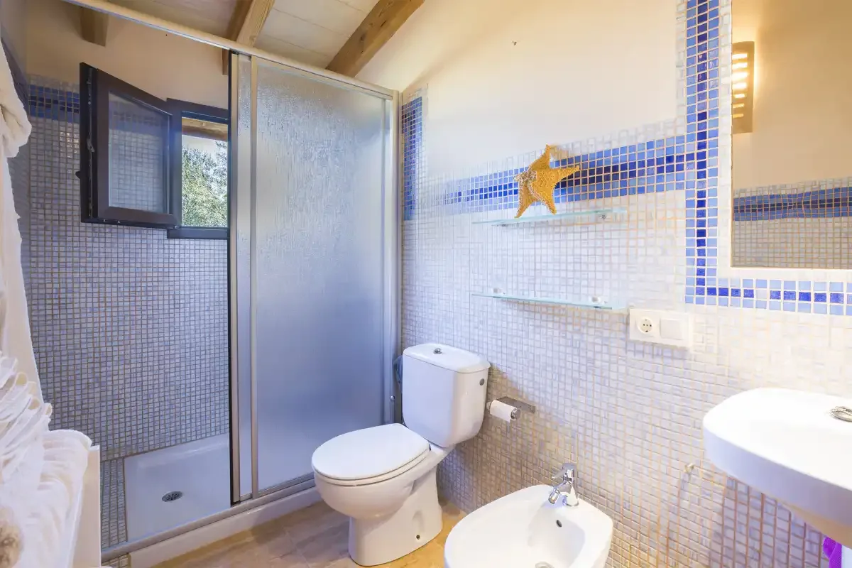 Un baño con azulejos, ducha, inodoro, lavabo y una ventana pequeña.