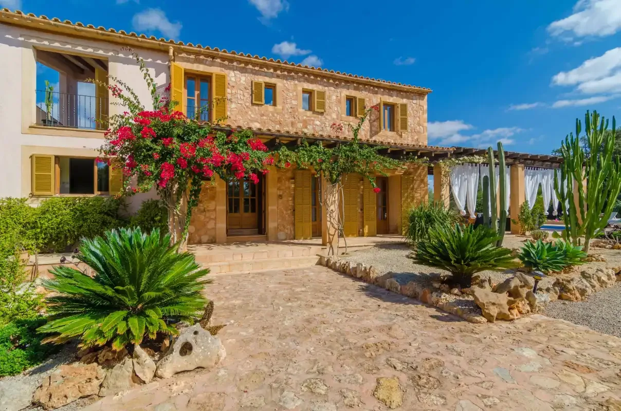 Una casa de piedra con patio pavimentado, enredaderas floridas y plantas desérticas.