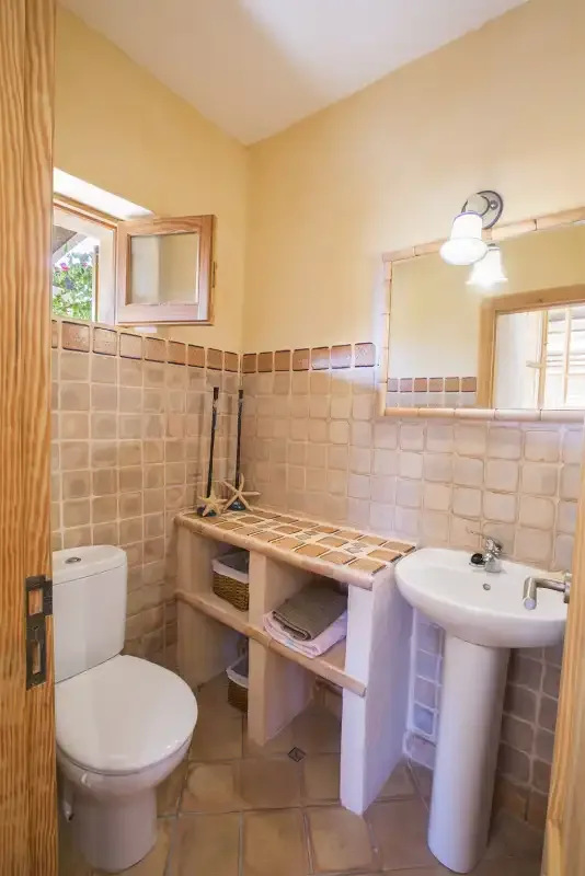Un baño alicatado con inodoro, lavabo y estantes abiertos.