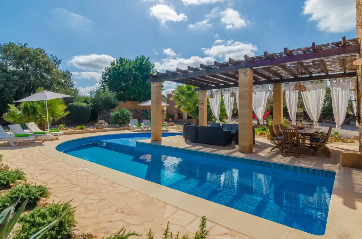 Una piscina al aire libre junto a una zona de estar sombreada por una pérgola.