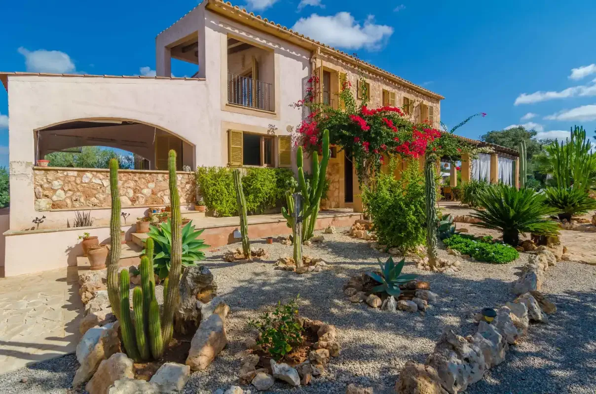 Una casa de estilo mediterráneo con enredaderas floridas y cactus en un jardín de grava.