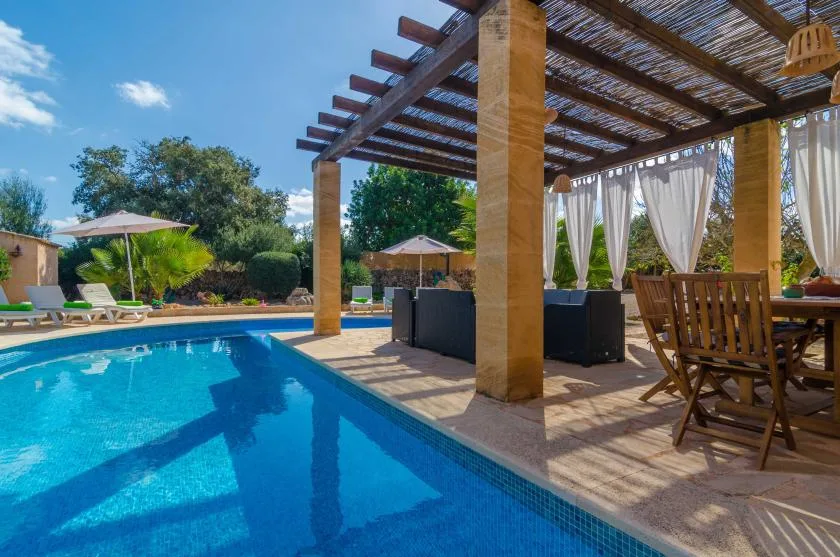Una piscina al aire libre junto a un patio sombreado con asientos para comer.