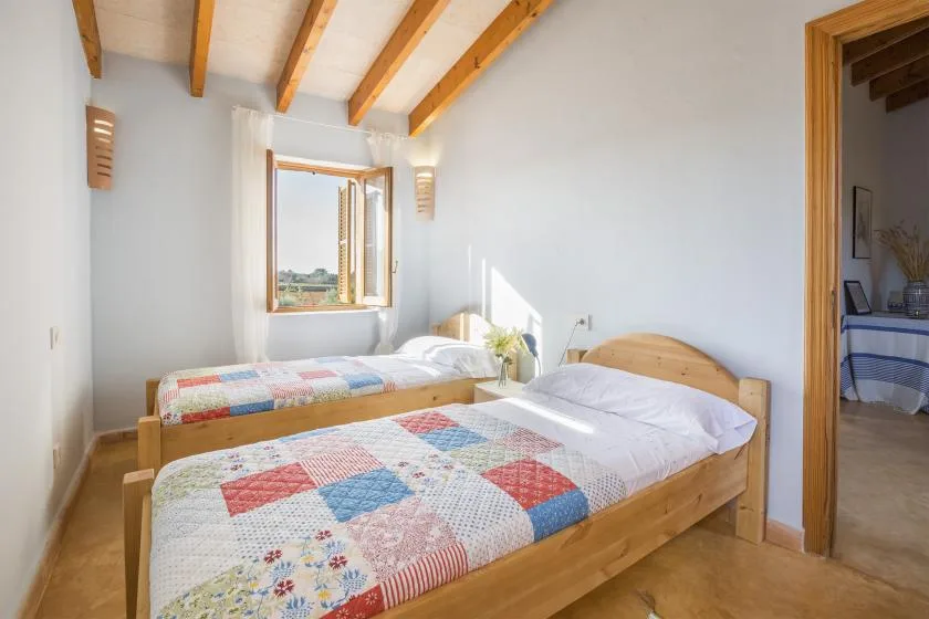 Un dormitorio luminoso con dos camas de madera cubiertas con colchas de retazos coloridas.