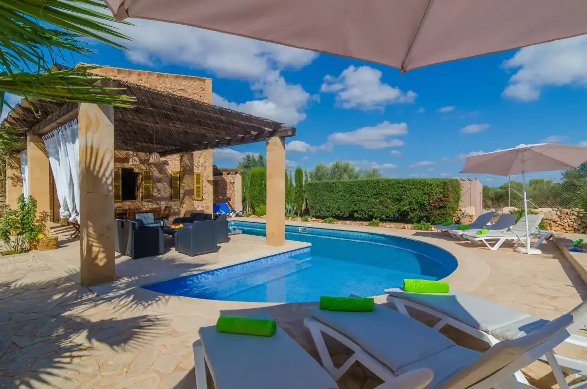 Una piscina al aire libre junto a un patio cubierto, con tumbonas y sombrillas.