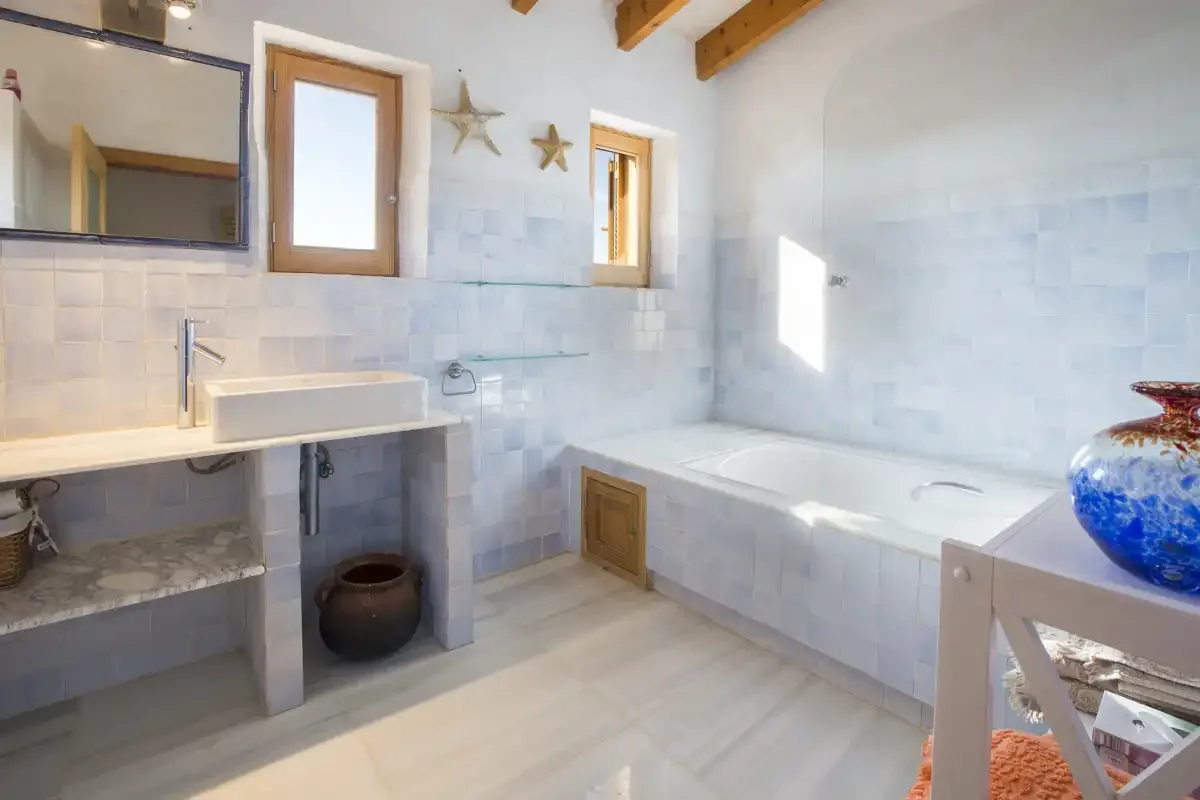 Un baño luminoso con azulejos, lavabo y bañera integrada.