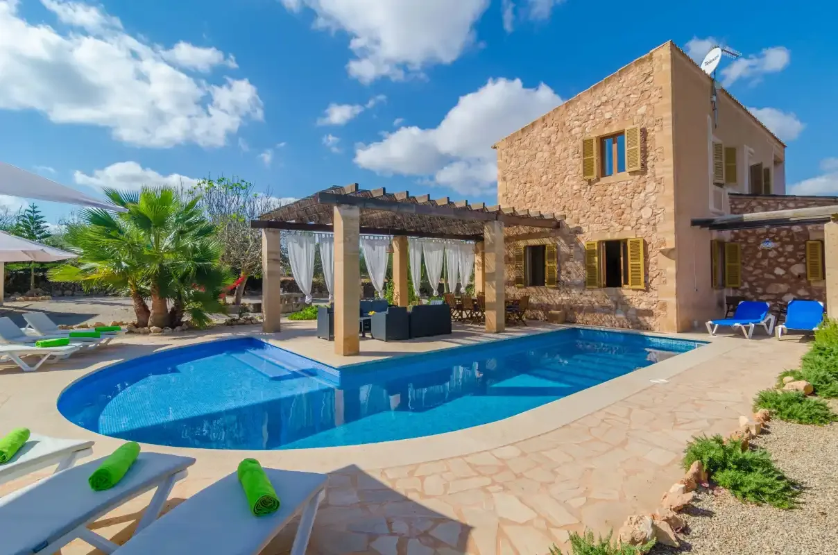 Una piscina junto a una casa de piedra y una zona de descanso a la sombra.