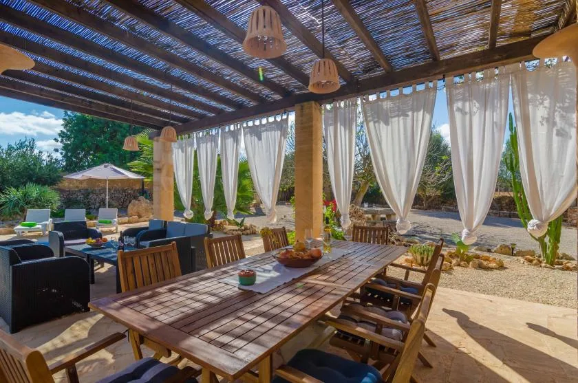 Una zona exterior sombreada para comer y sentarse, con cortinas abiertas hacia un jardín.