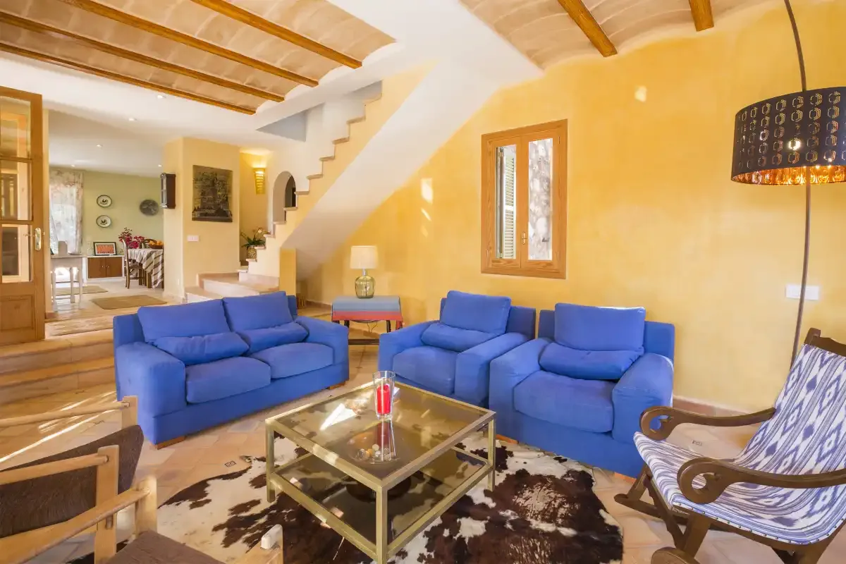 Una sala de estar con asientos azules, una mesa de centro de vidrio y una escalera.