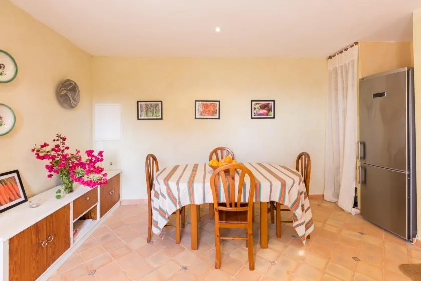 Un comedor con un mantel a rayas, sillas de madera y un refrigerador.