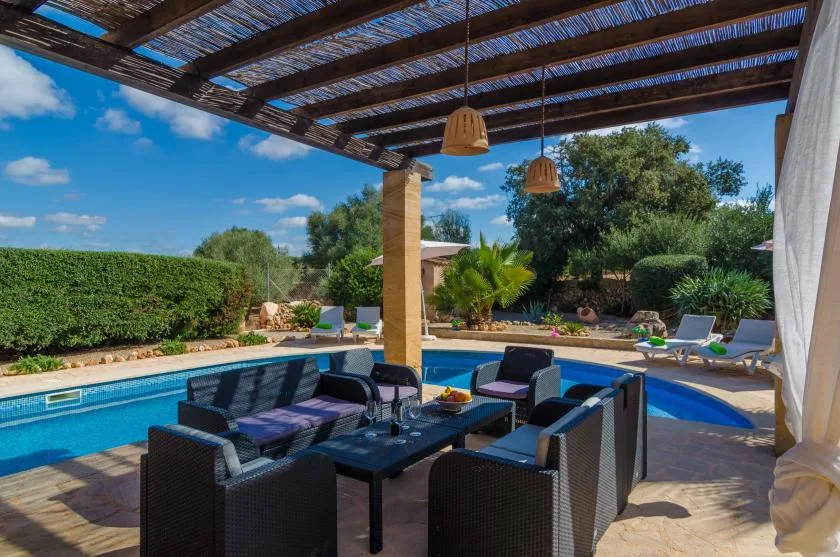 A shaded outdoor seating area overlooks a swimming pool and garden.