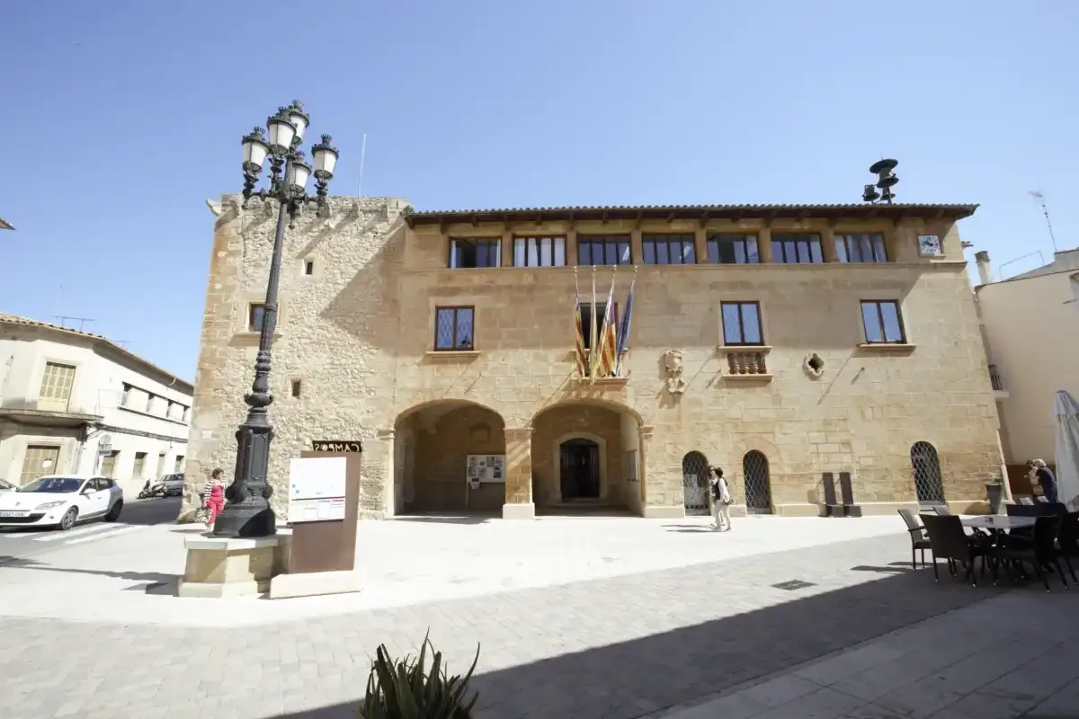 Un antiguo edificio público de piedra da a una plaza pavimentada y soleada.