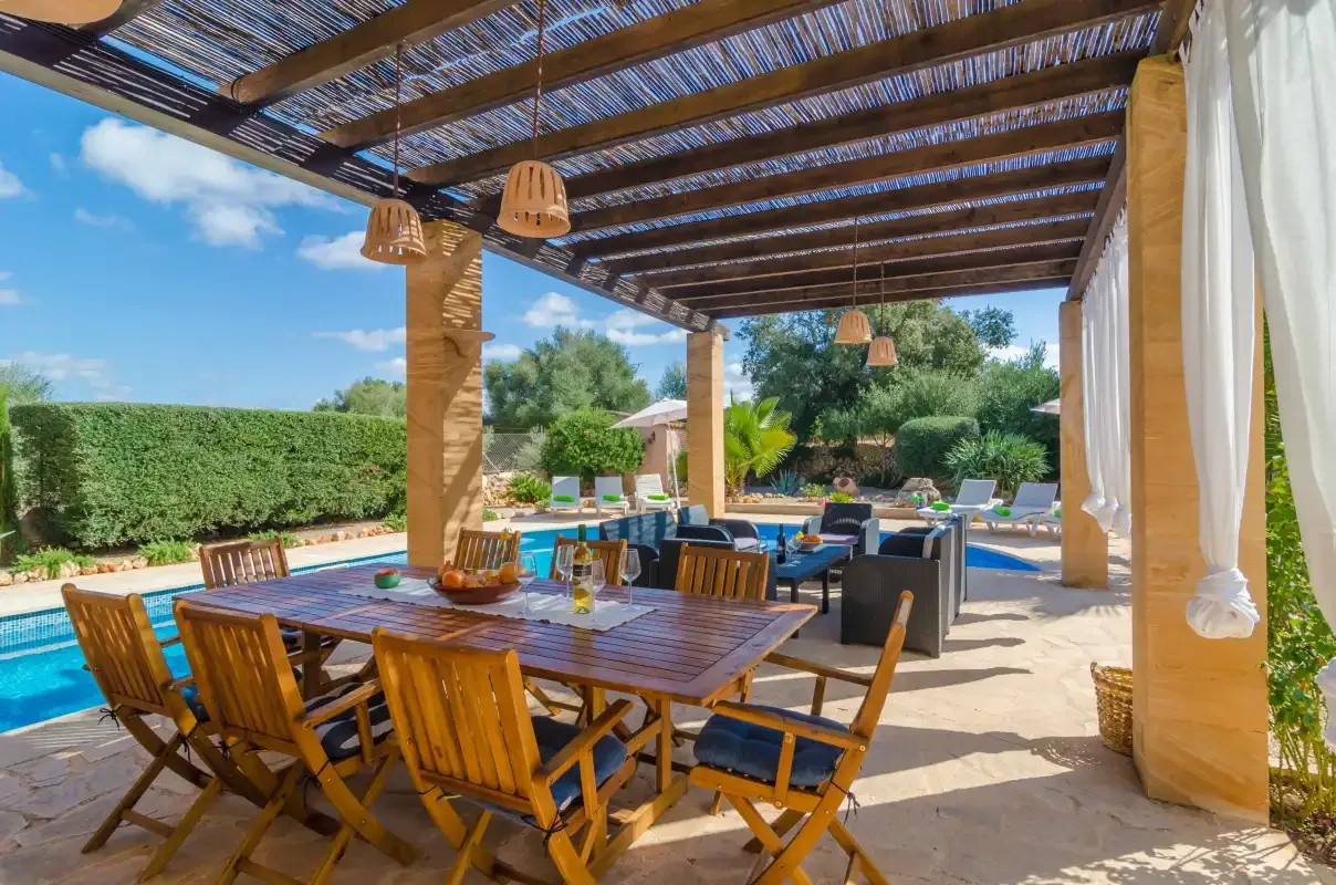 Comedor exterior cubierto con asientos de madera junto a una piscina.