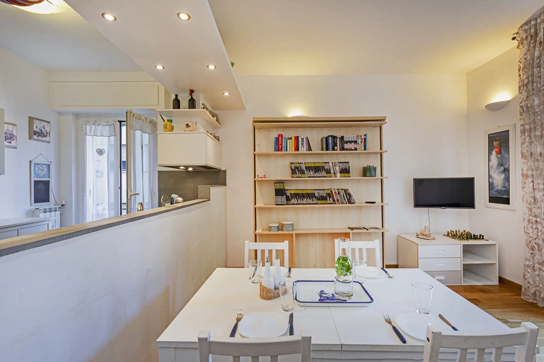 Un comedor luminoso con una mesa, estanterías abiertas y un televisor.