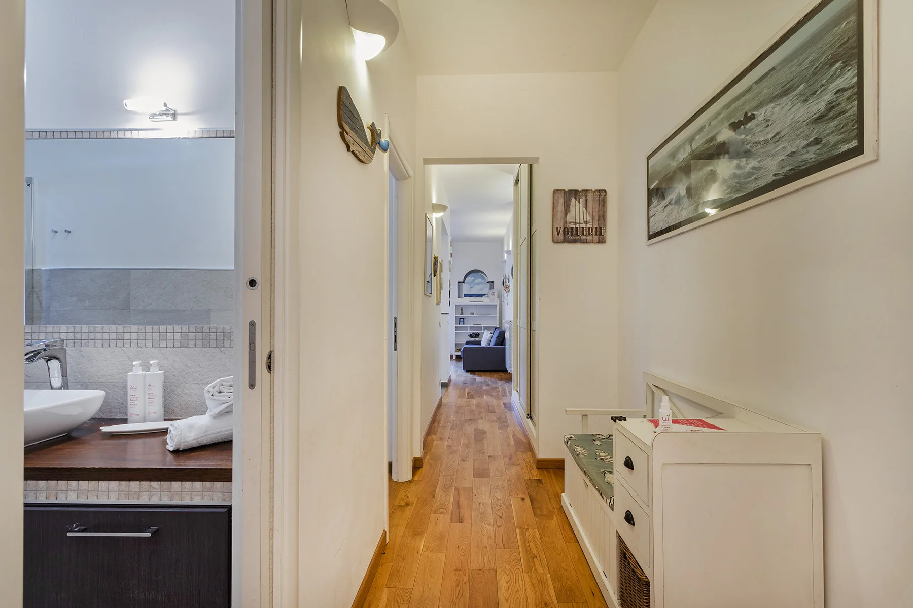 Un pasillo estrecho con suelo de madera conduce a una habitación amueblada.