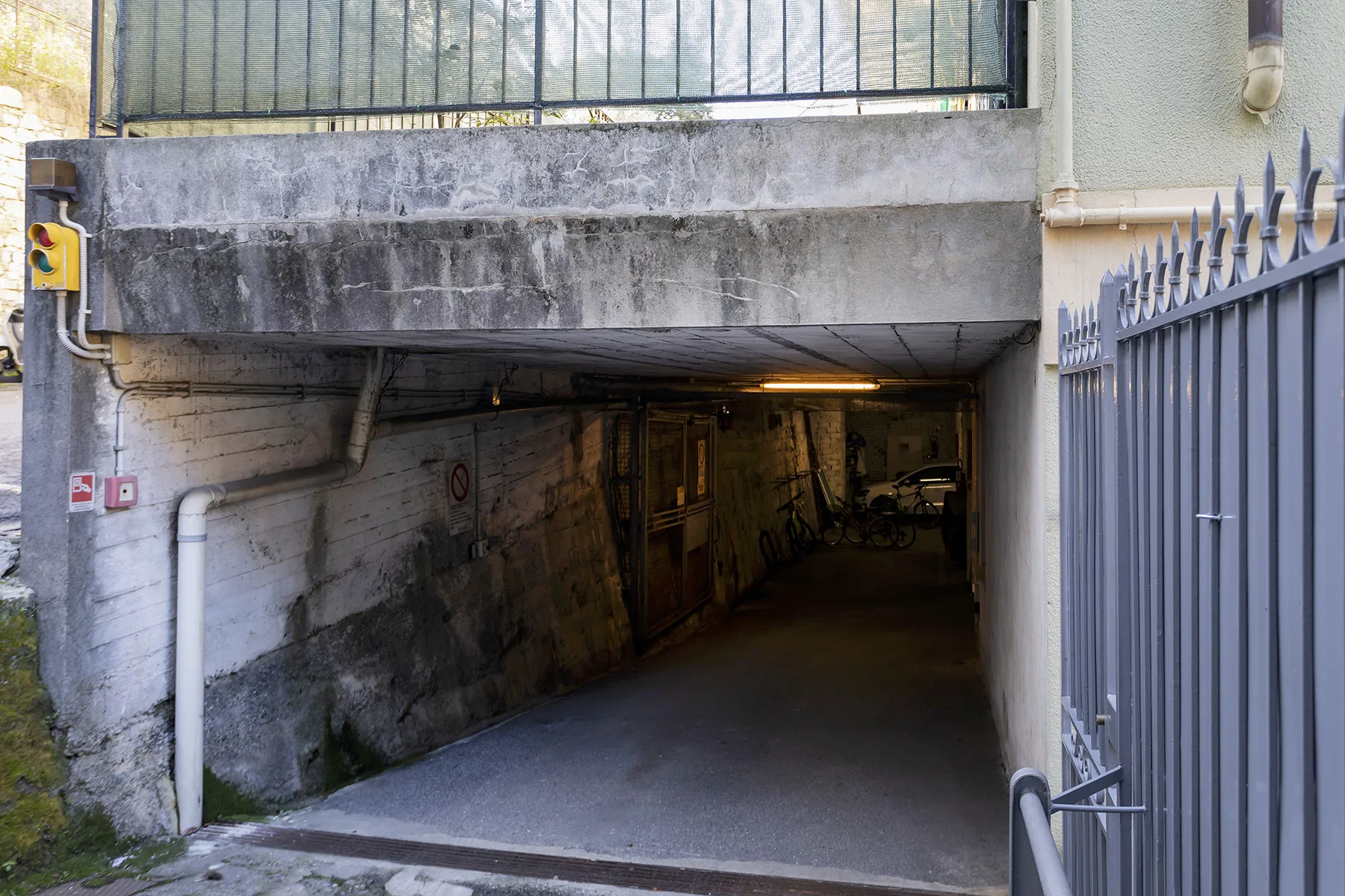 Un pasaje subterráneo oscuro pasa bajo una estructura de hormigón, con una reja metálica en la entrada.