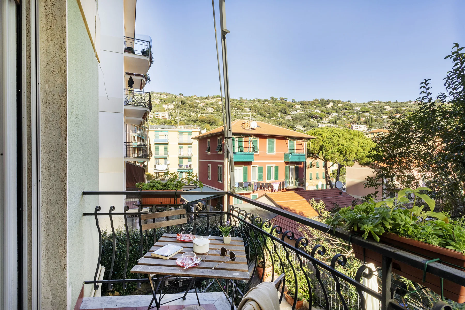 Un balcón con una pequeña mesa de comedor da a edificios coloridos y una ladera.