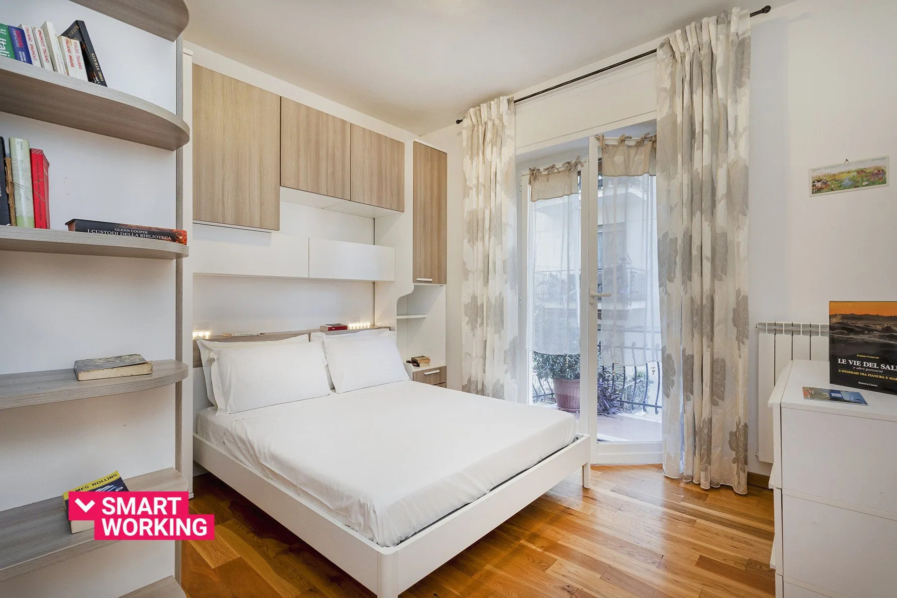 Un dormitorio luminoso con una cama, estanterías empotradas y puertas de vidrio que dan a un balcón.
