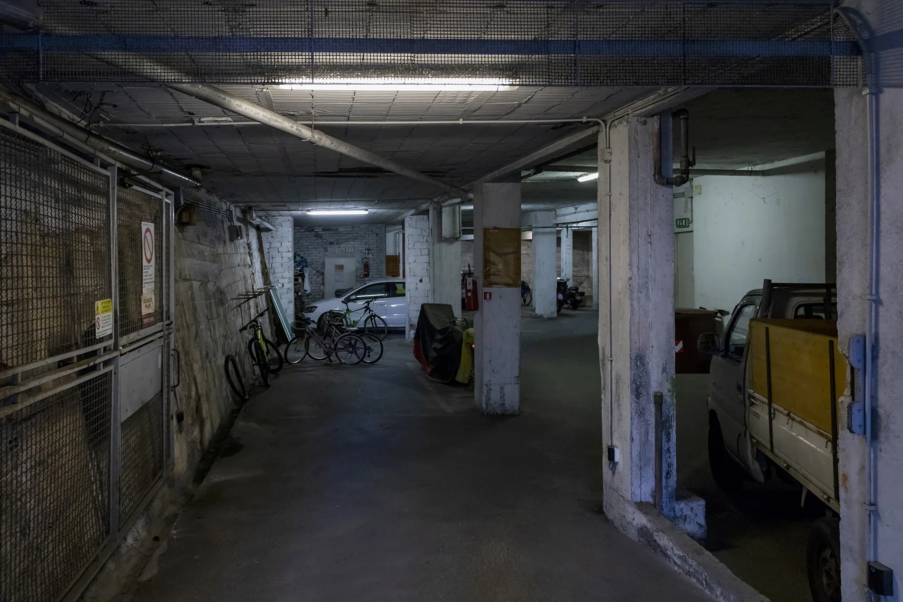 Un área de estacionamiento interior con bicicletas y vehículos junto a columnas de concreto.